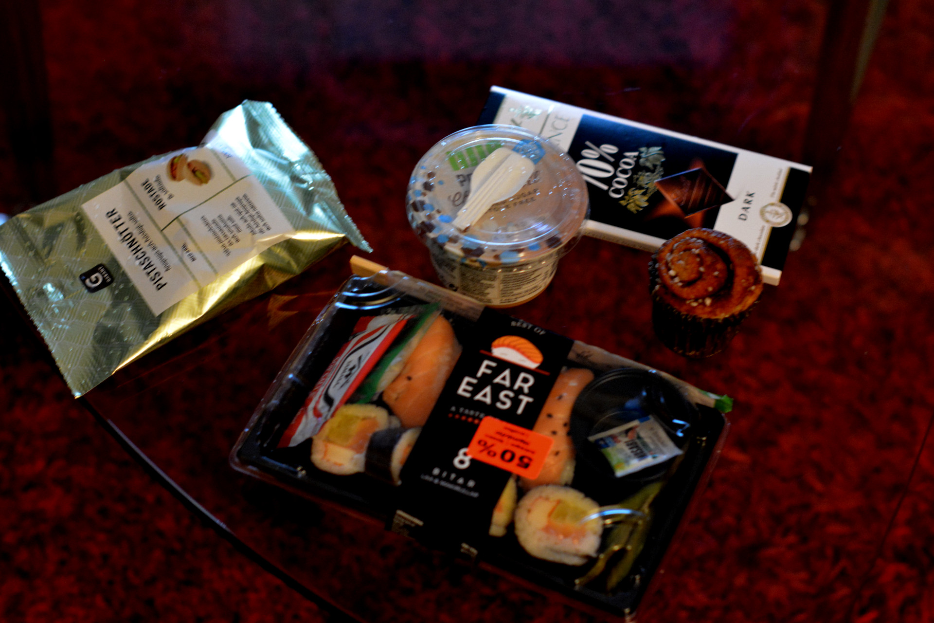 Sushi, pistagenötter, kanelbulle, proteinpudding och mörk choklad på ett bord.