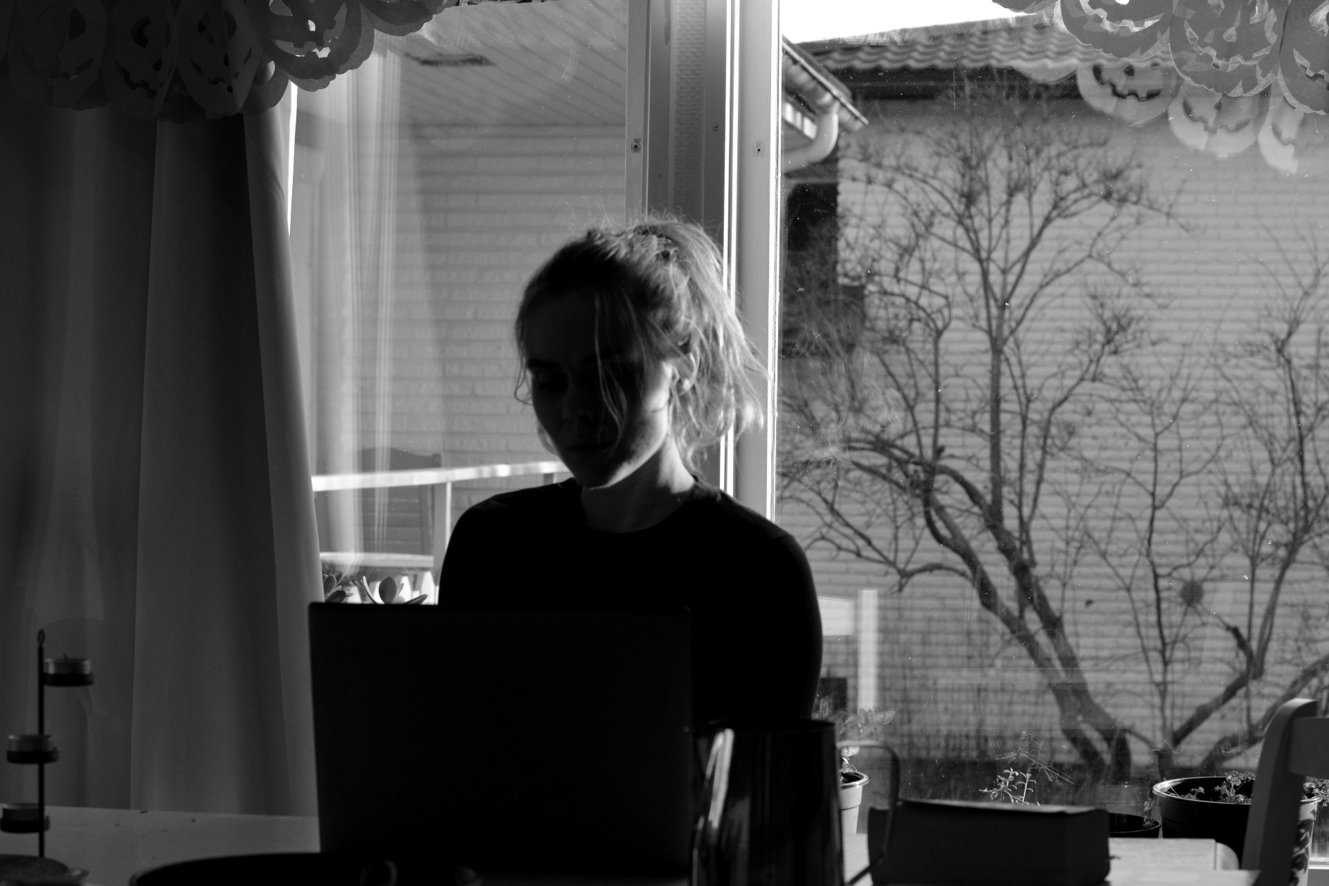 Svartvit bild på Ulrika Nettelblad som skriver på laptop i motljus.