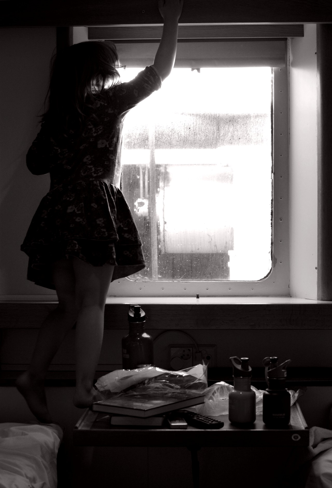 Svartvit bild på flicka som tittar ut genom fönster på hytt på Eckerölinjen.
