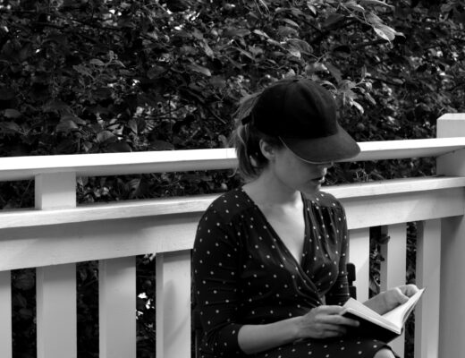 Ulrika Nettelblad läser en bok på balkong. Svartvit bild.