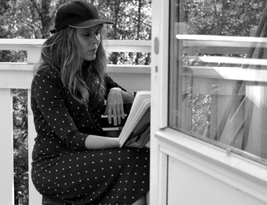 Svartvit bild på Ulrika Nettelblad som läser bok på en balkong